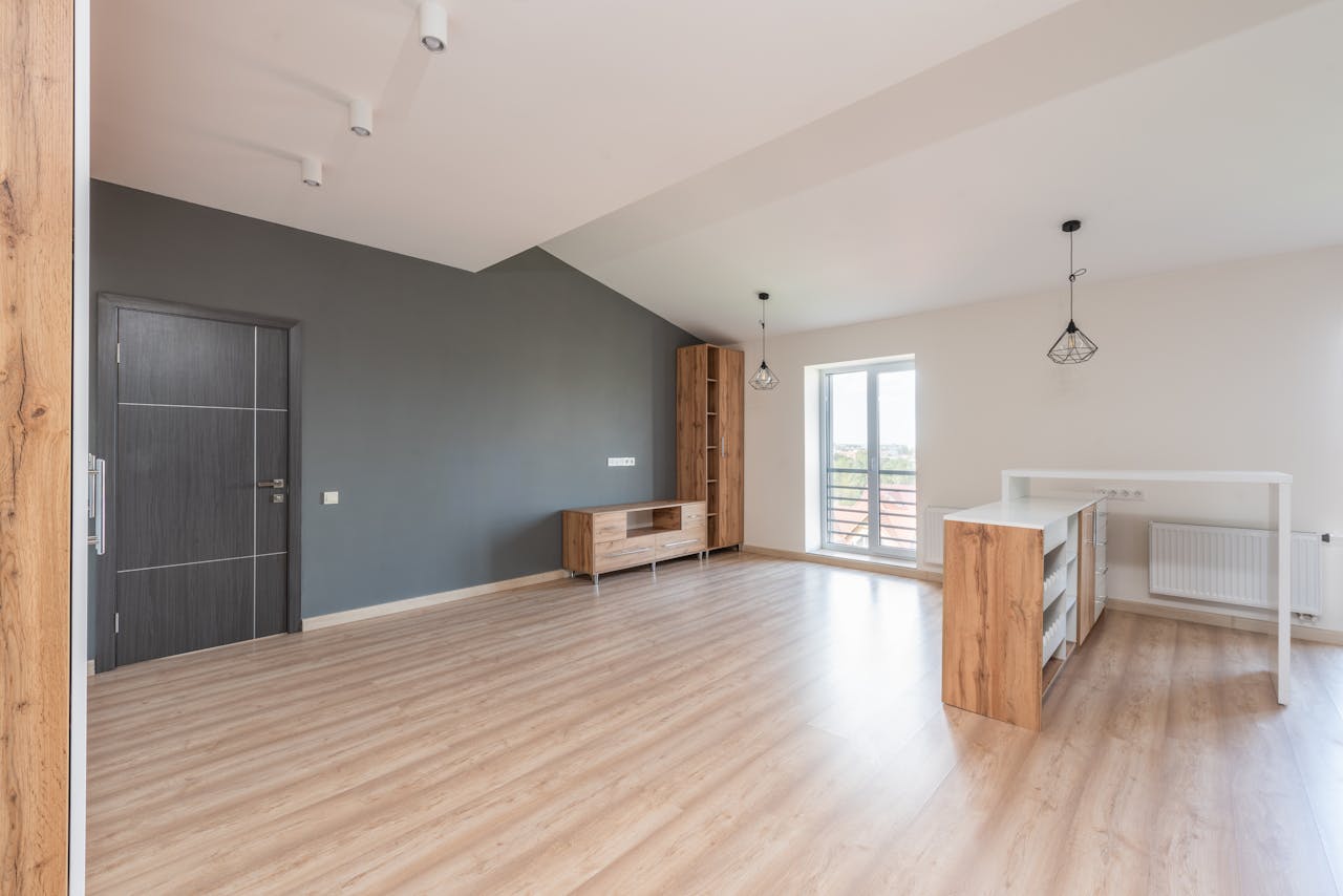 Spacious modern living room featuring wooden flooring, gray accent wall, and natural light.